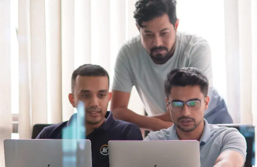 Three data engineers working together with two laptops on AI/ML solutions.