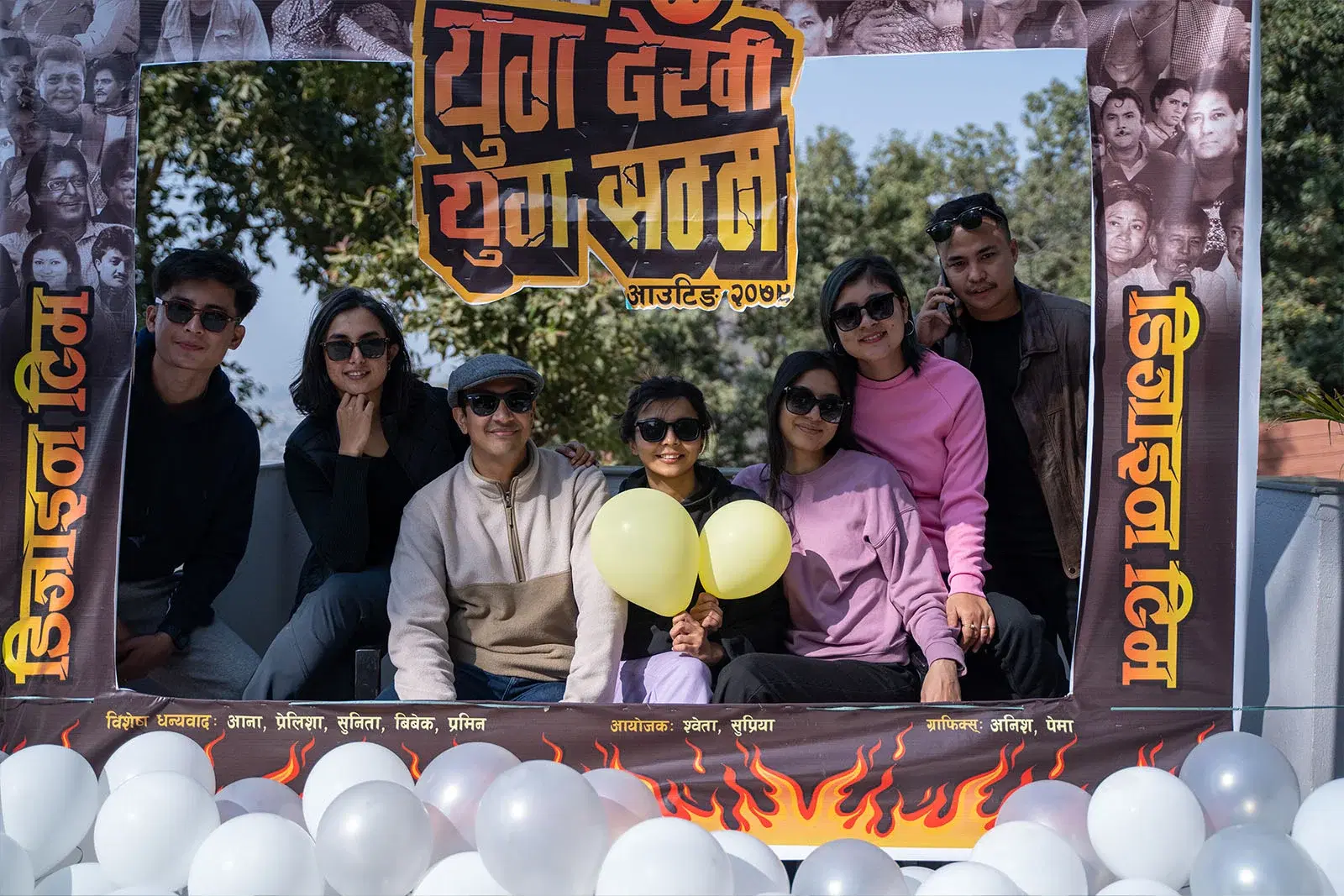 A group picture of seven people posing in a Nepali movie-themed photo booth.
